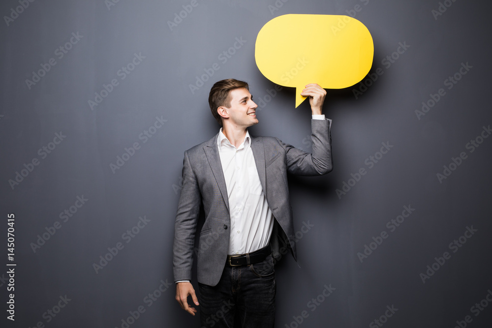 Young beautiful man holding a yellow bubble for text, isolated on a grey background Young beautiful man holding a yellow bubble for text, isolated on a grey background