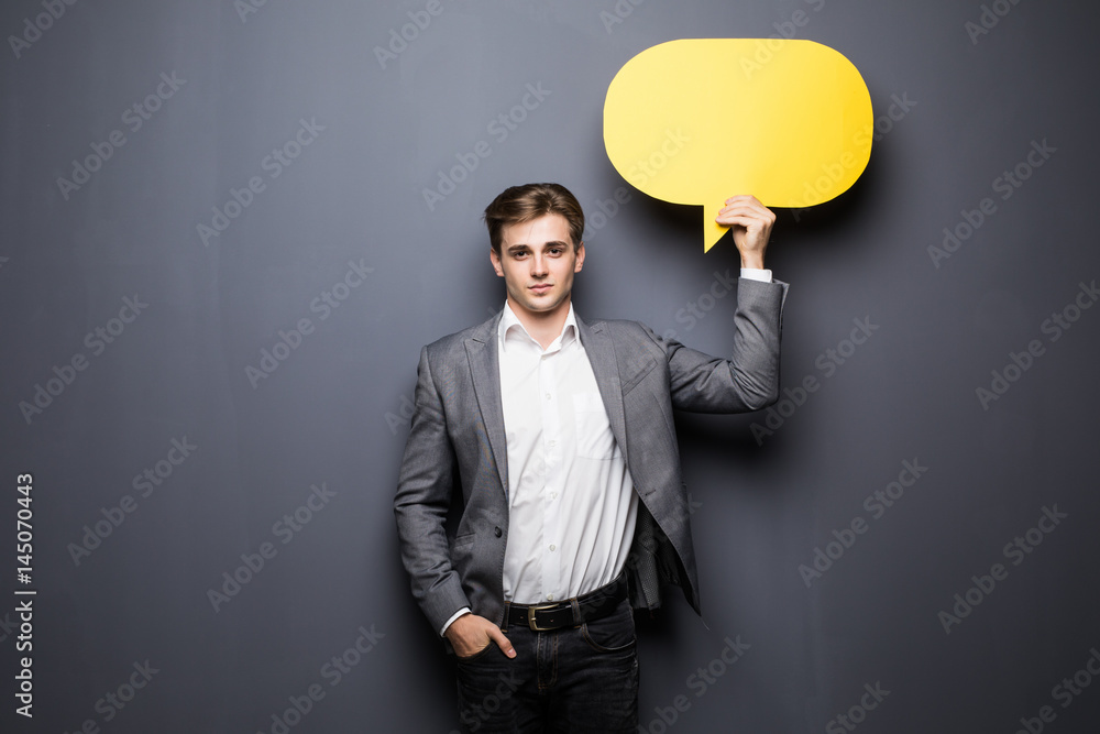 Young beautiful man holding a yellow bubble for text, isolated on a grey background Young beautiful man holding a yellow bubble for text, isolated on a grey background