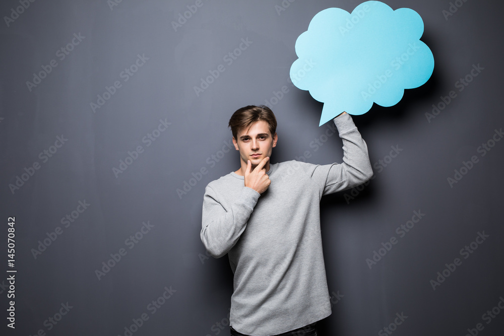 Man with hands on chin holding blue blank speech bubble with space for text on grey background Man with hands on chin holding blue blank speech bubble with space for text on grey background