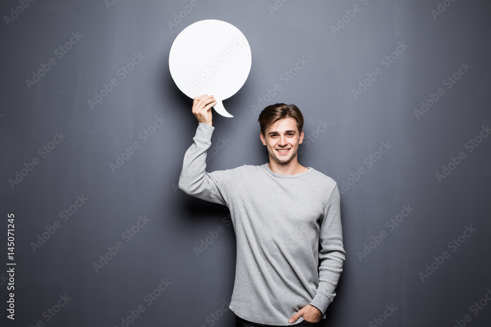 Young smile man holding white blank speech bubble with space for text isolated on grey background. Young smile man holding white blank speech bubble with space for text isolated on grey background.