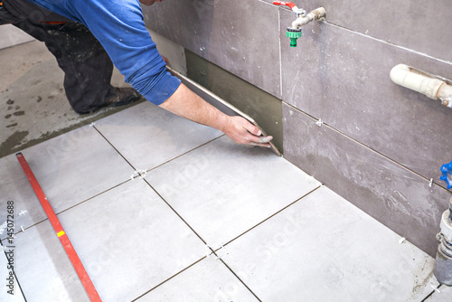 Tiling Floor & Wall. The tiler builder arranges the bathroom ceramics. Laying tiles on the floor