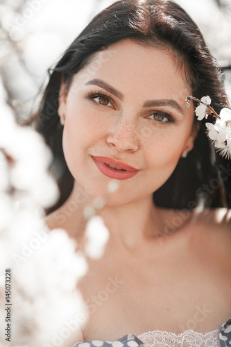 Portrait of young woman among blooming branches of apricot tree.