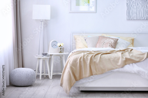 Quadro su tela Comfortable bed with soft beige coverlet and pillows in light modern room