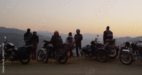 A group of motorcyclists rest and look at the sunset with the Himalayas