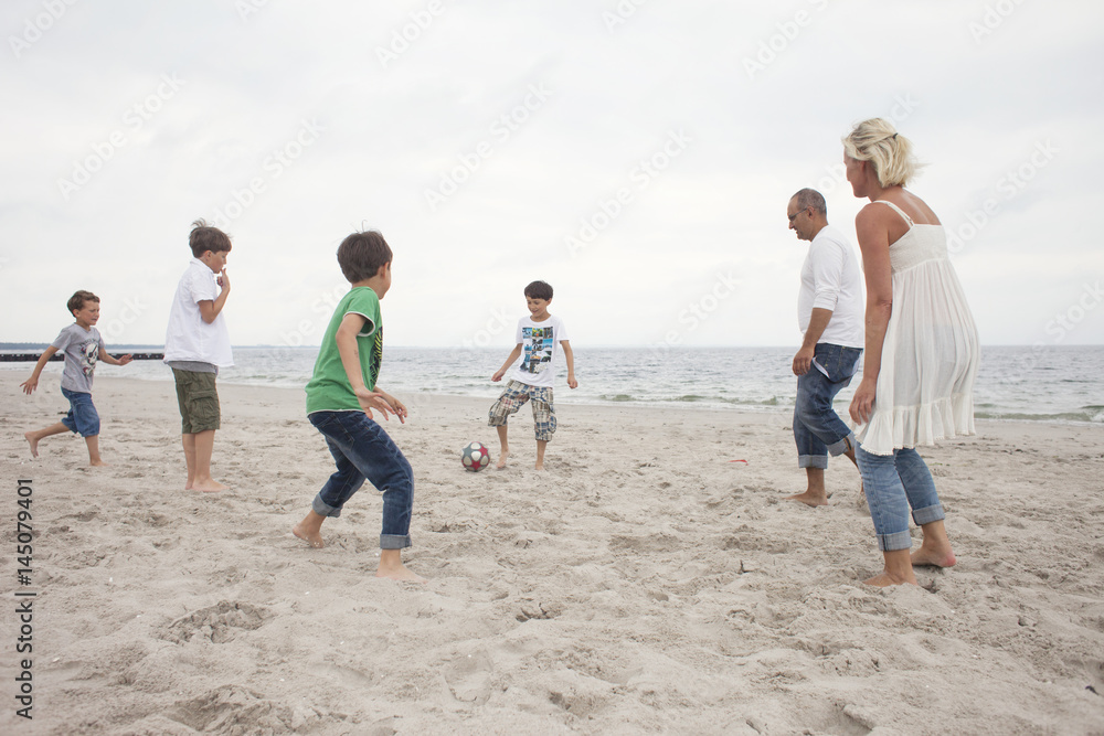 Family playing soccer at beach against sky Family playing soccer at beach against sky