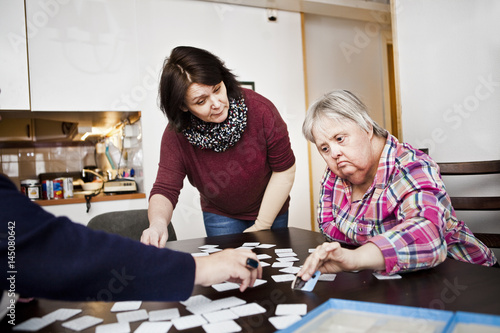 Healthcare worker assisting women with down syndrome in arranging cards at table photo