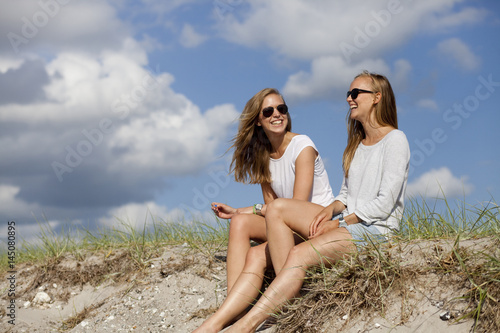 Cheerful friends sitting on sand at beach against sky