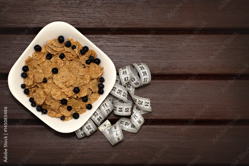 Corn flakes with berries in white plate on brown wooden boards. Nearby lies a meter. Background, texture, close-up. View from above Corn flakes with berries in white plate on brown wooden boards. Nearby lies a meter. Background, texture, close-up. View from above