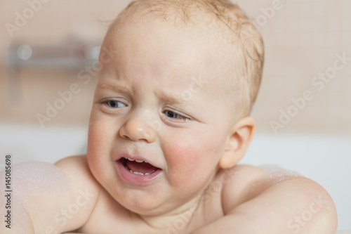 Tearful infant kid an a bathtub. Crying toddler boy taking a bath
