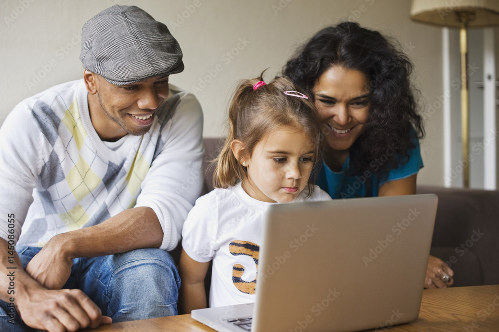 Happy father and mother with daughter using laptop at home Happy father and mother with daughter using laptop at home