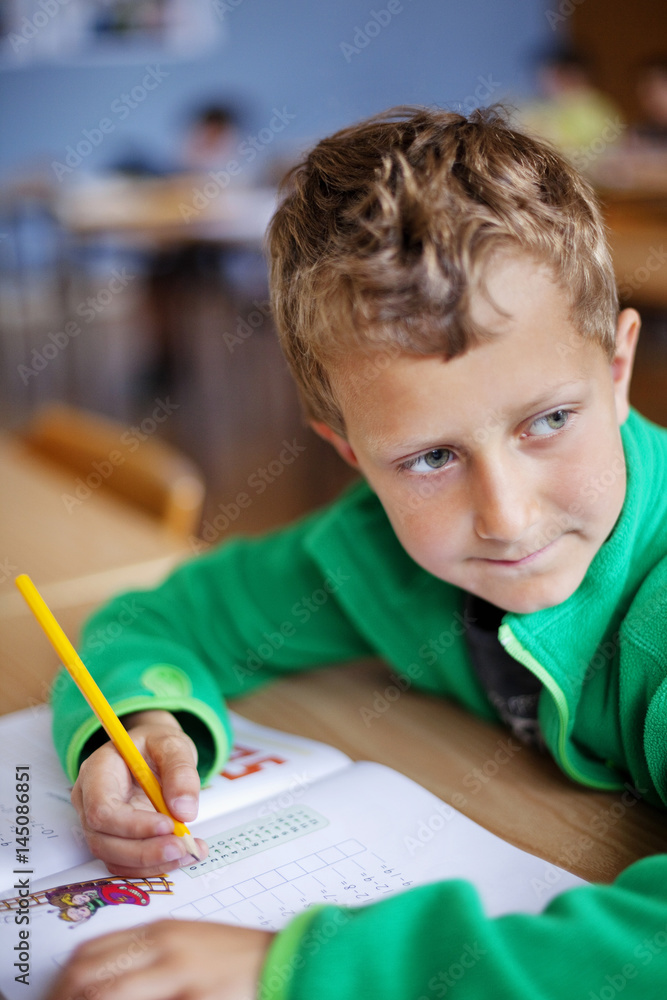 Blond boy sitting with book and pencil while looking away in classroom Blond boy sitting with book and pencil while looking away in classroom
