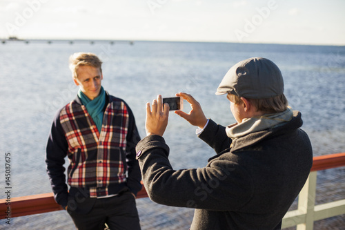 Man photographing gay partner on pier against sea photo