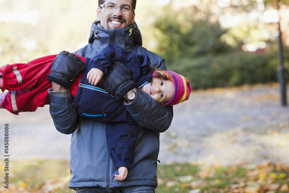 Portrait of playful father carrying daughter at park Portrait of playful father carrying daughter at park