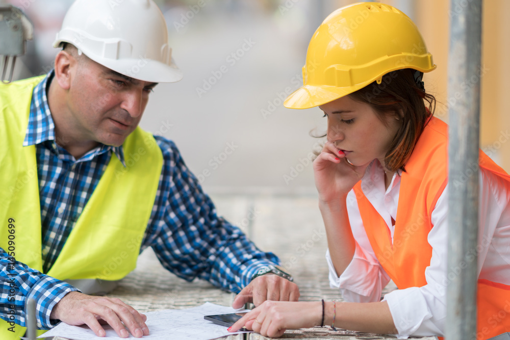 Two construction engineers holding plans and inspecting the construction site Two construction engineers holding plans and inspecting the construction site