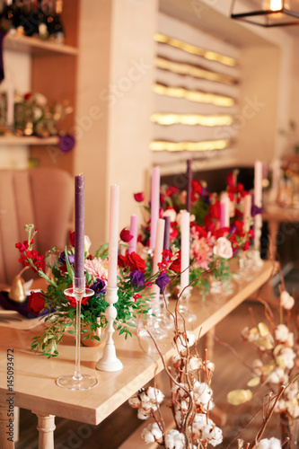 decorated wooden table with candles in glass candle holders, fruits in gold paint and a beautiful bottle of red and white flowers