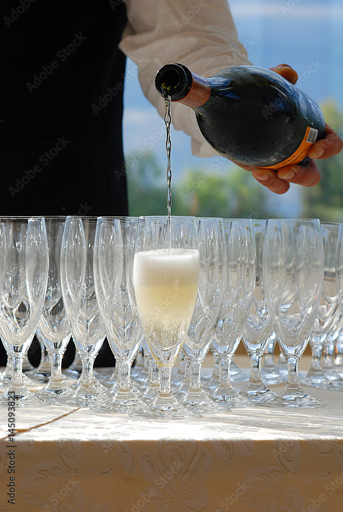 cameriere versa aperitivo alcolico in bicchiere di vetro in mezzo ad altri  bicchieri vuotibicchieri a calice in vetro Photos | Adobe Stock