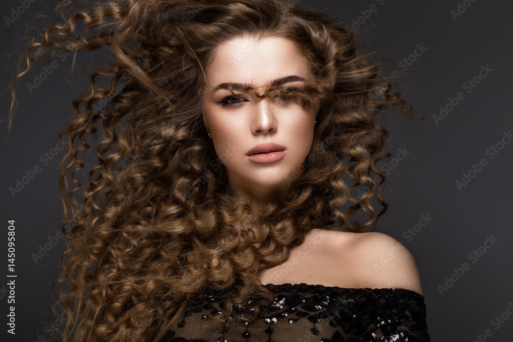 Beautiful brunette girl in move with a perfectly curly hair, and classic make-up. Beauty face. Picture taken in the studio on grey background. Beautiful brunette girl in move with a perfectly curly hair, and classic make-up. Beauty face. Picture taken in the studio on grey background.