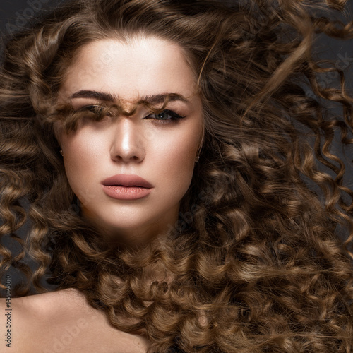 Beautiful brunette girl in move with a perfectly curly hair, and classic make-up. Beauty face. Picture taken in the studio on grey background.