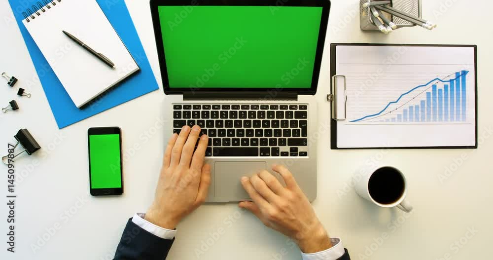 Business man working with laptop and smartphone with green screen on white office desk. Top view. Chroma key Business man working with laptop and smartphone with green screen on white office desk. Top view. Chroma key