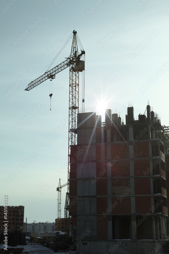 Fototapeta premium Under construction high-rise building with yellow construction crane in the sunlight