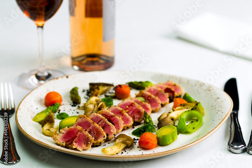 Salad of tuna and vegetables with a glass of wine and a bottle of wine on a white tablecloth, studio light