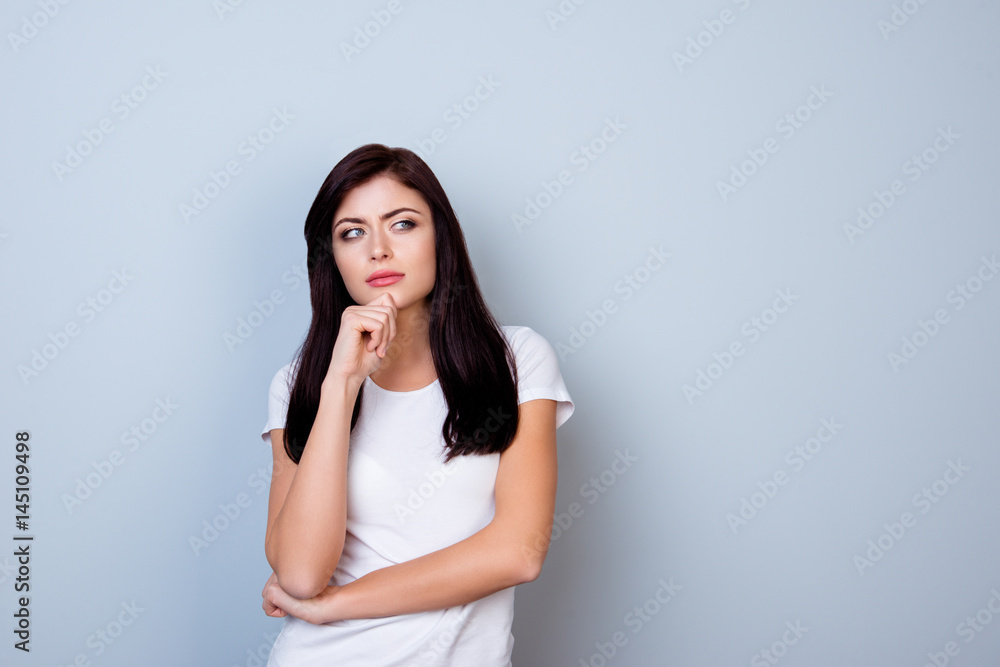 Portrait of young minded woman in white t-shirt touching her chin isolated on gray background Portrait of young minded woman in white t-shirt touching her chin isolated on gray background