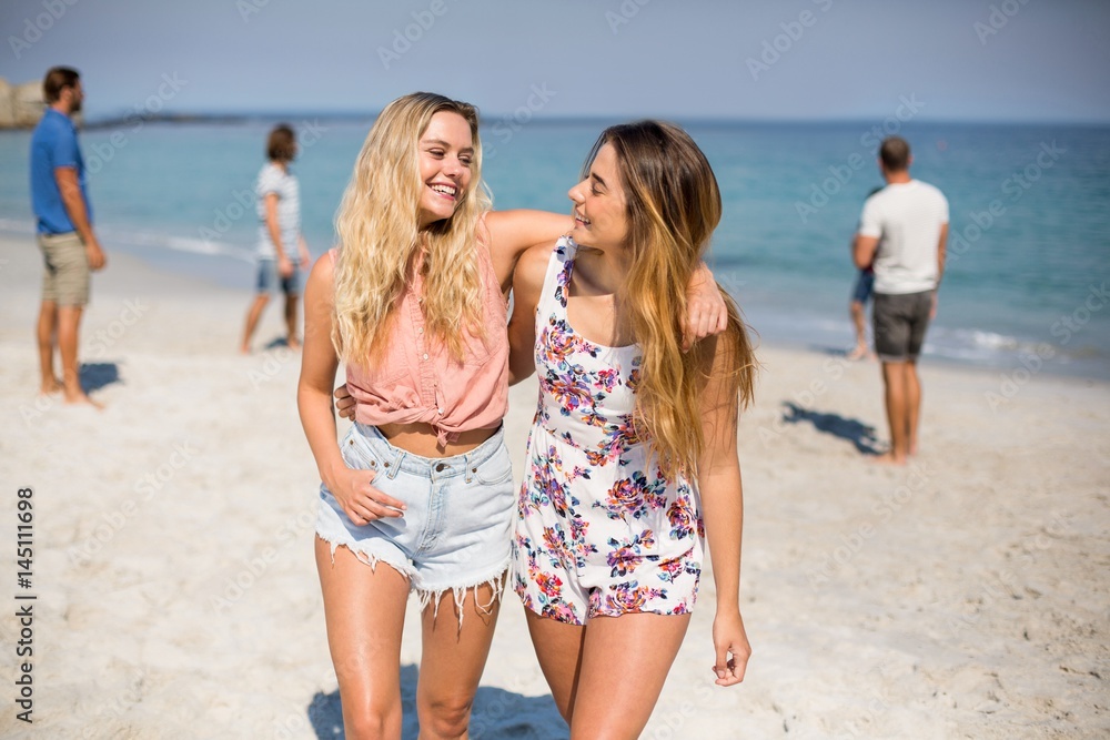 Friends with arm around walking on shore at beach Friends with arm around walking on shore at beach