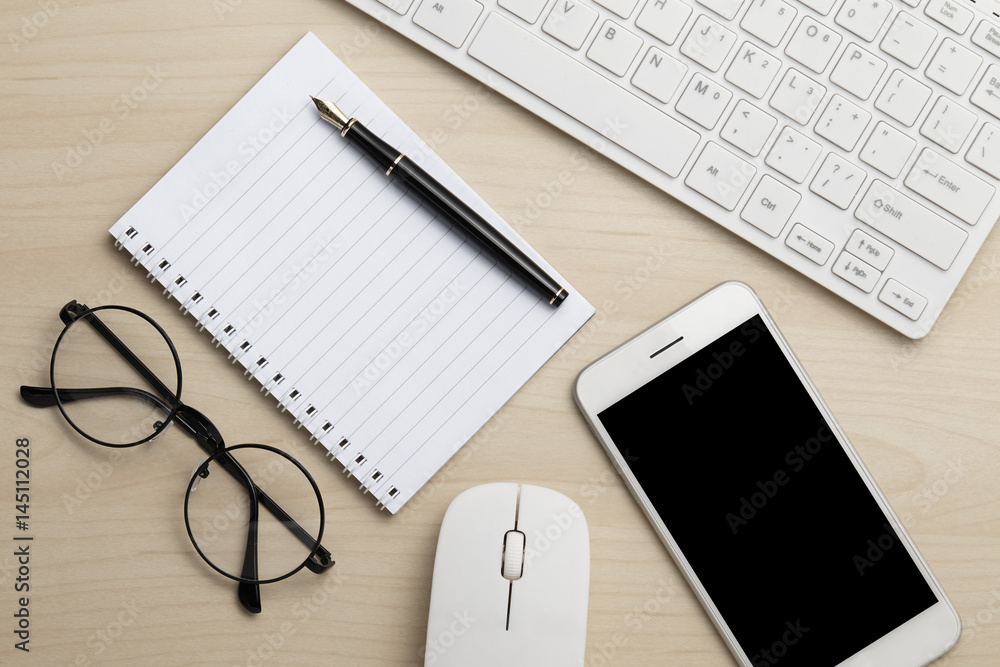 Modern working business desk with keyboard, notepad, smart phone, pen, mouse & glasses. Top view with copy space Modern working business desk with keyboard, notepad, smart phone, pen, mouse & glasses. Top view with copy space