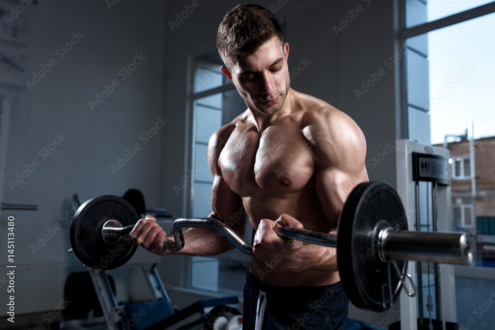 Young muscular man in shorts with a barbell trains in the gym close-up Young muscular man in shorts with a barbell trains in the gym close-up