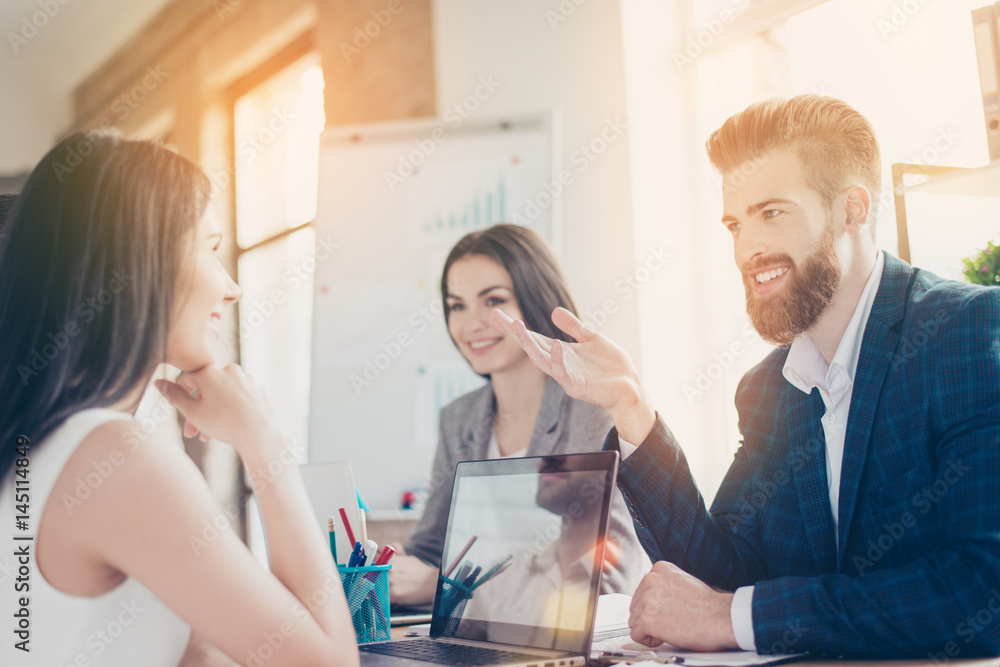 Business partners are smiling and discussing documents and ideas to solve problems of the company at meeting in bright workstation Business partners are smiling and discussing documents and ideas to solve problems of the company at meeting in bright workstation