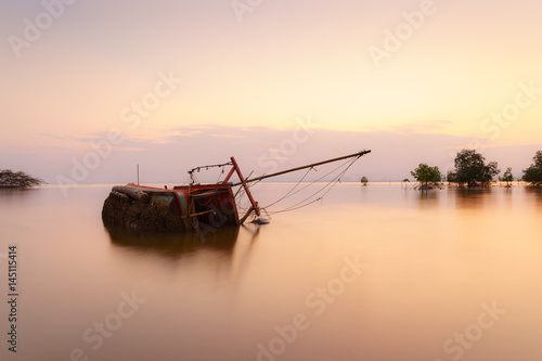 The old  boat capsized on sea at sunset