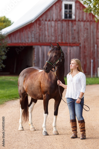 Young woman standing with horse in front of a barn