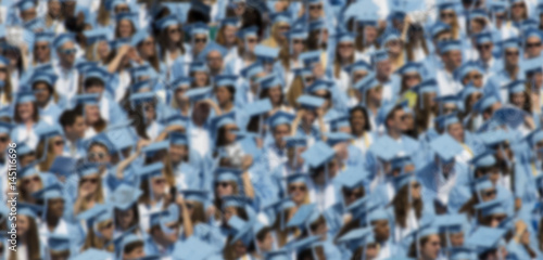 Unrecognizable blurred focus graduates in light blue caps and gowns background