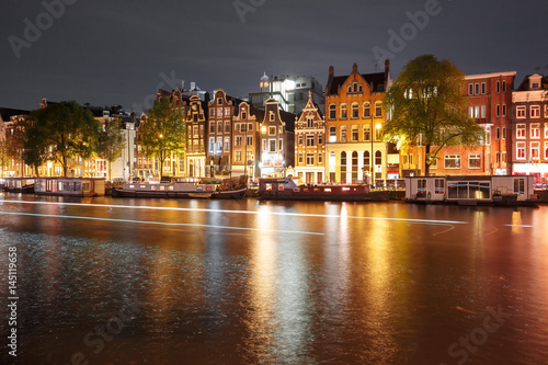 Amsterdam canal Amstel with typical dutch houses, houseboat and luminous track from the boat at night, Holland, Netherlands.