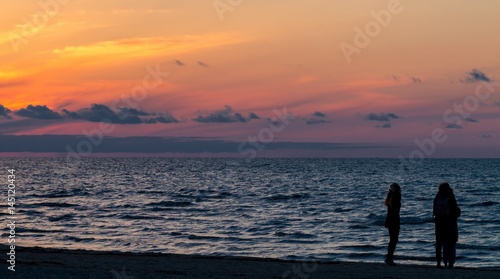 Jurmala (Riga), Latvia - April 16, 2017: Golden sunset on the Baltic sea with silhouettes of people (shadows). Coastal landscape with setting Sun reflections on the water and sand (in Latvia)