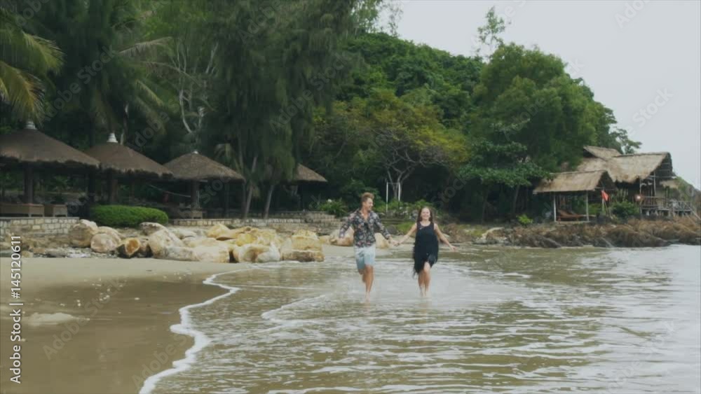Young couple in love running on the sea beach holding hands, smiling and laughing in slow motion. The concept of a happy family and rest