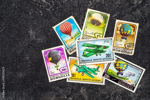 Set of randomly lying postage stamps printed in Mongolia shows balloons and airplanes, series, circa 1976-1982. Copy space for your text on a dark black cement background.