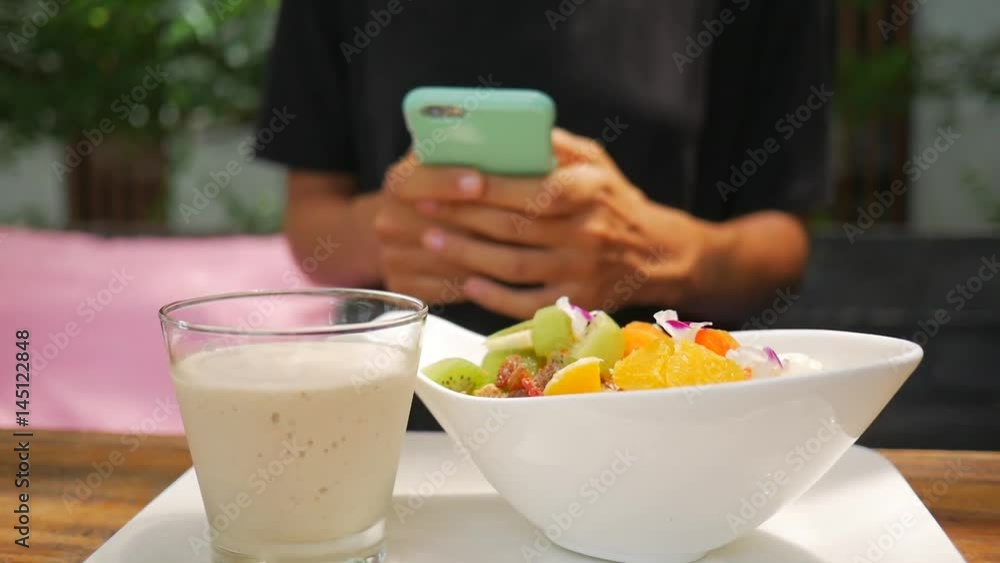 Female Twxting with Mobile Phone During her Healthy Vegan Breakfast. Close up of a Young Girl Hands Using Smartphone. HD. Female Twxting with Mobile Phone During her Healthy Vegan Breakfast. Close up of a Young Girl Hands Using Smartphone. HD.