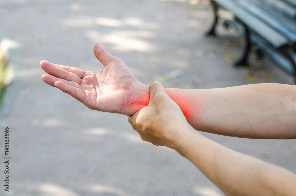 Fototapeta premium Pain in a man wrist. Male holding hand to spot of wrist pain in the park