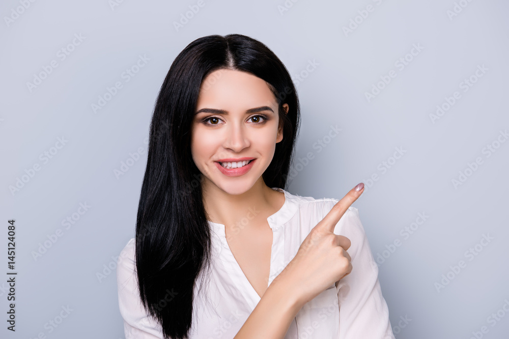 Portrait of beautiful cute smiling young woman with black hair pointing at copy space Portrait of beautiful cute smiling young woman with black hair pointing at copy space