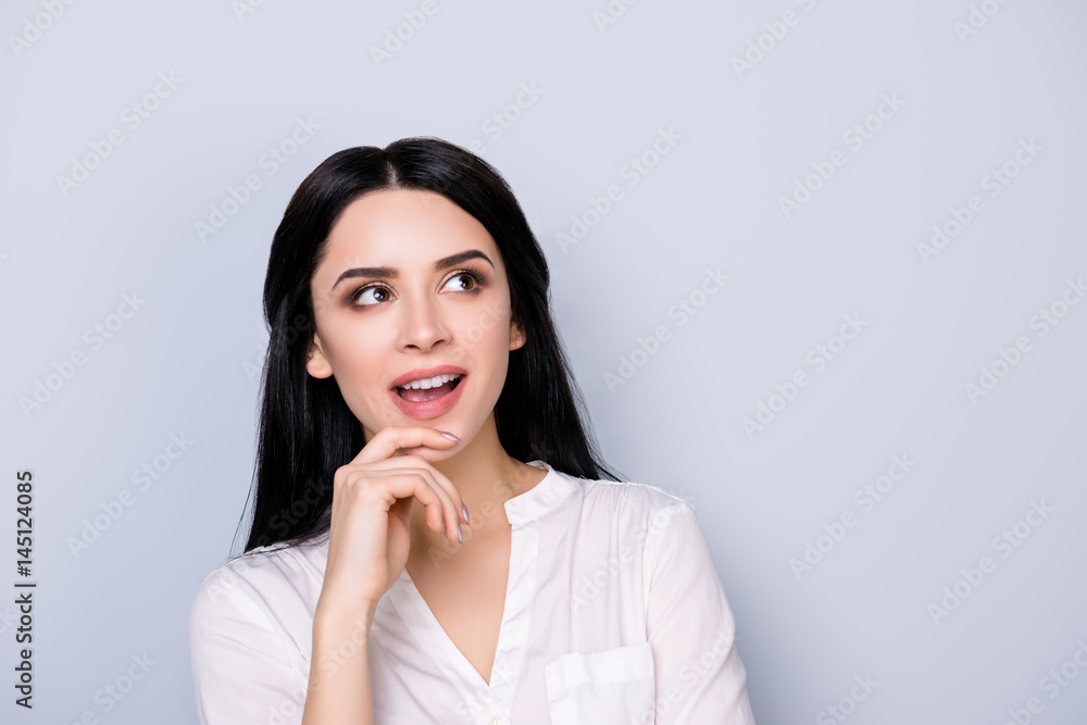 Close up portrait of beautiful cute young woman in formalwear with black hair fink about new idea and looking at copy space on gray background Close up portrait of beautiful cute young woman in formalwear with black hair fink about new idea and looking at copy space on gray background