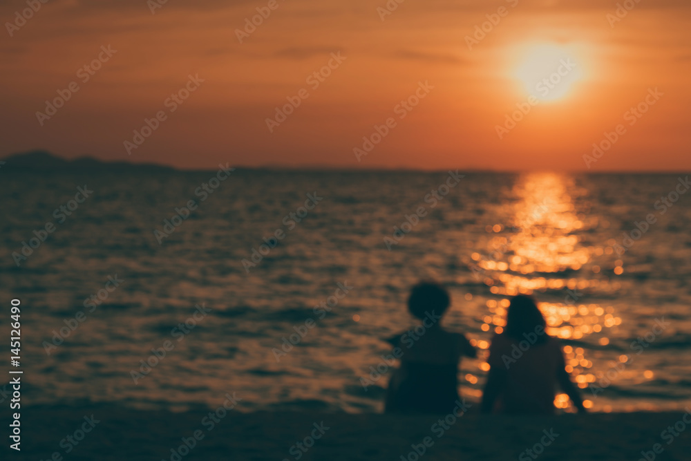 silhouette and blur of two middle-aged happy women sitting on the beach talking about old day and watching the sunset on the horizon. emotional and friend relation concept. 