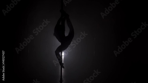 Young woman's silhouette dancing near the pole in the dark room