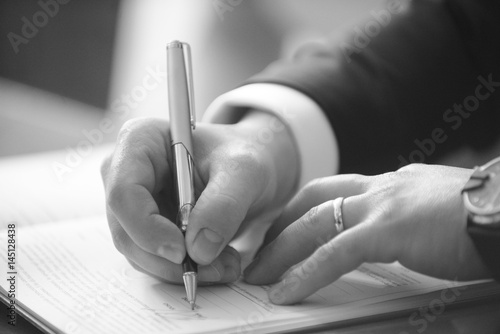 foto b/n di una mano che firma con una penna un documento