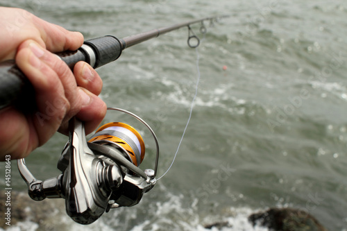 Close-up of fishing reel in hand with the ocean in the background.