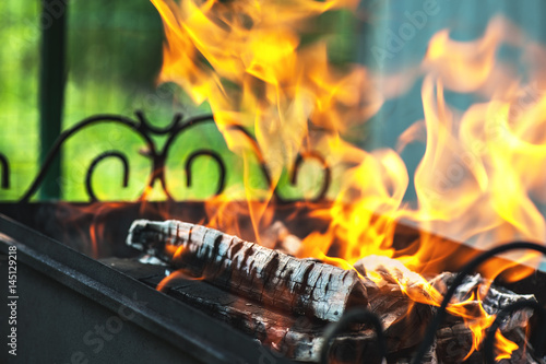 burning wood in a metal barbecue with smoke and embers diagonally on a bright green background, horizontal frame