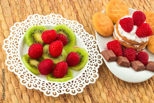 Fresh Red Raspberries on a white artistic plate   Red Fresh Raspberries on a white artistic plate with cookies  rosemary  chocolate and cream in the background.