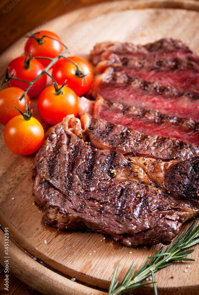 Sliced medium rare grilled Beef steak Ribeye with cherry tomatoes on cutting board, selective focus