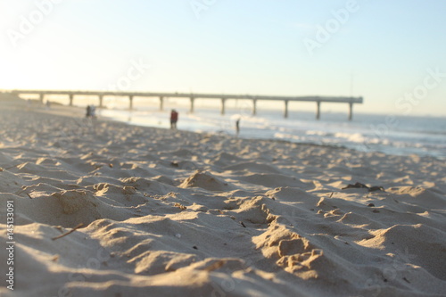 a sandy beach for people with shark rock pier in the back