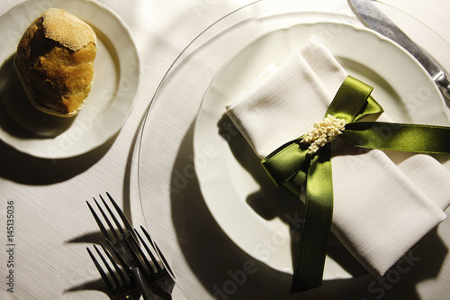 Apparecchiatura  sobria con piatti bianchi e fiocco verde intorno al  fazzoletto, piatto bianco con il pane photo
